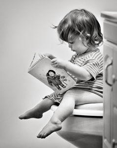 black and white photo of child reading book on toilet